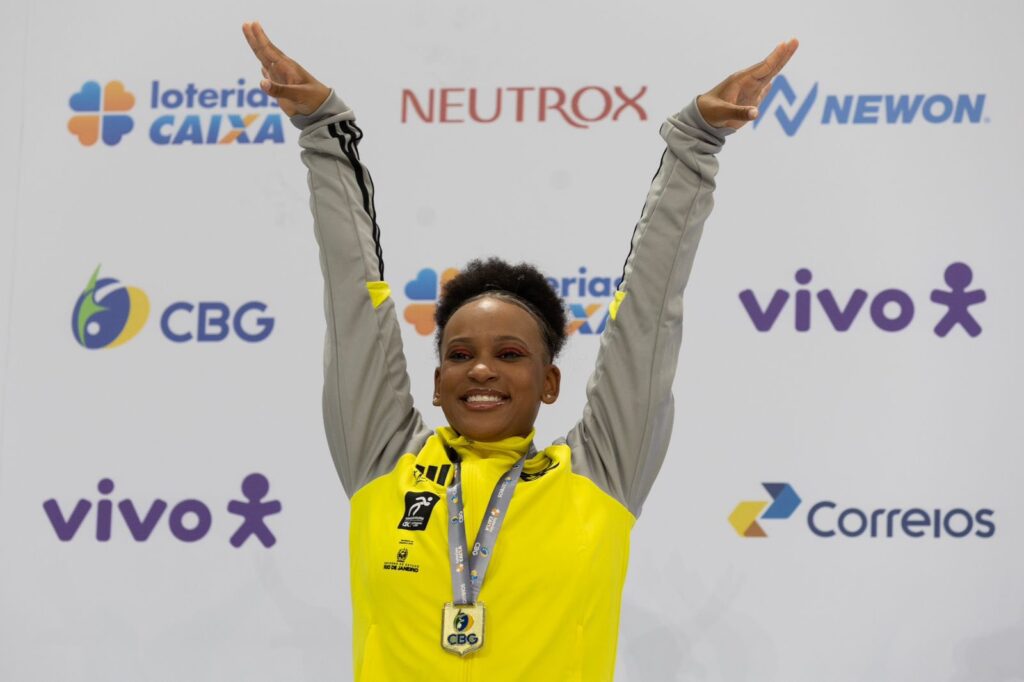 Com casaco do Flamengo, Rebeca Andrade posa com medalha de ouro no pódio do Troféu Brasil, último torneio antes das Olimpíadas