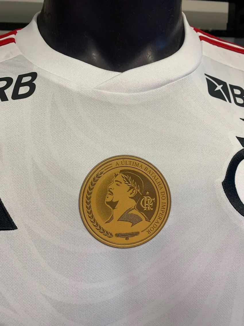 A camisa branca também apresenta um patch dourado na área central do peito