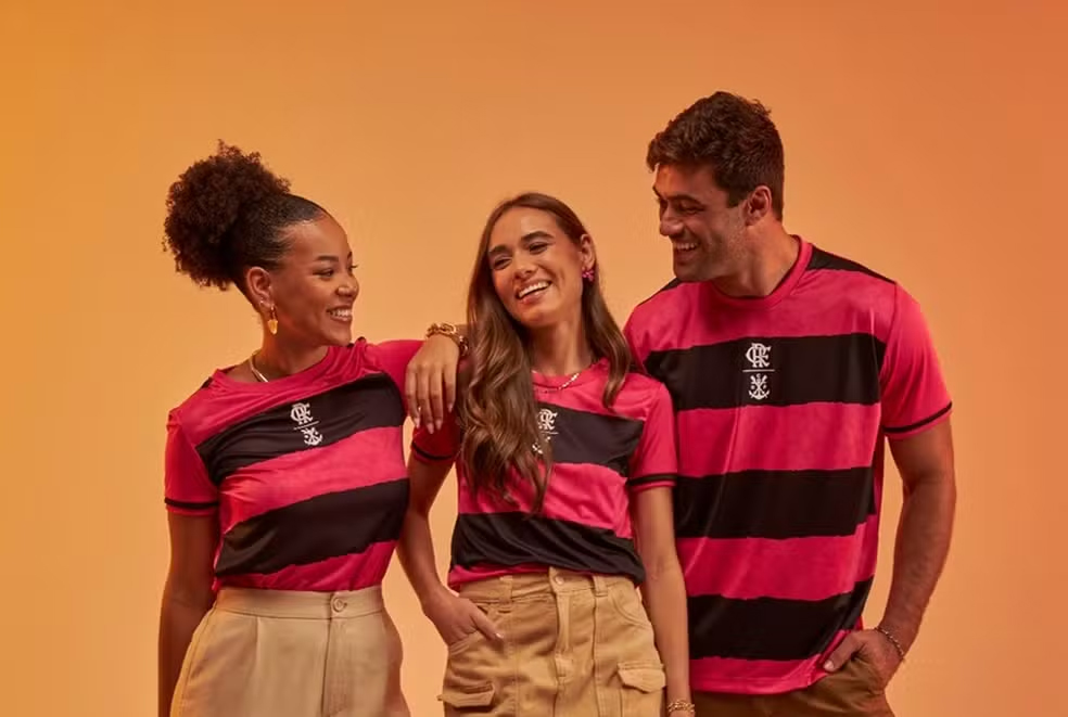 Um homem e duas mulheres vestindo a camisa rosa do Flamengo, feita pela Braziline em 2024